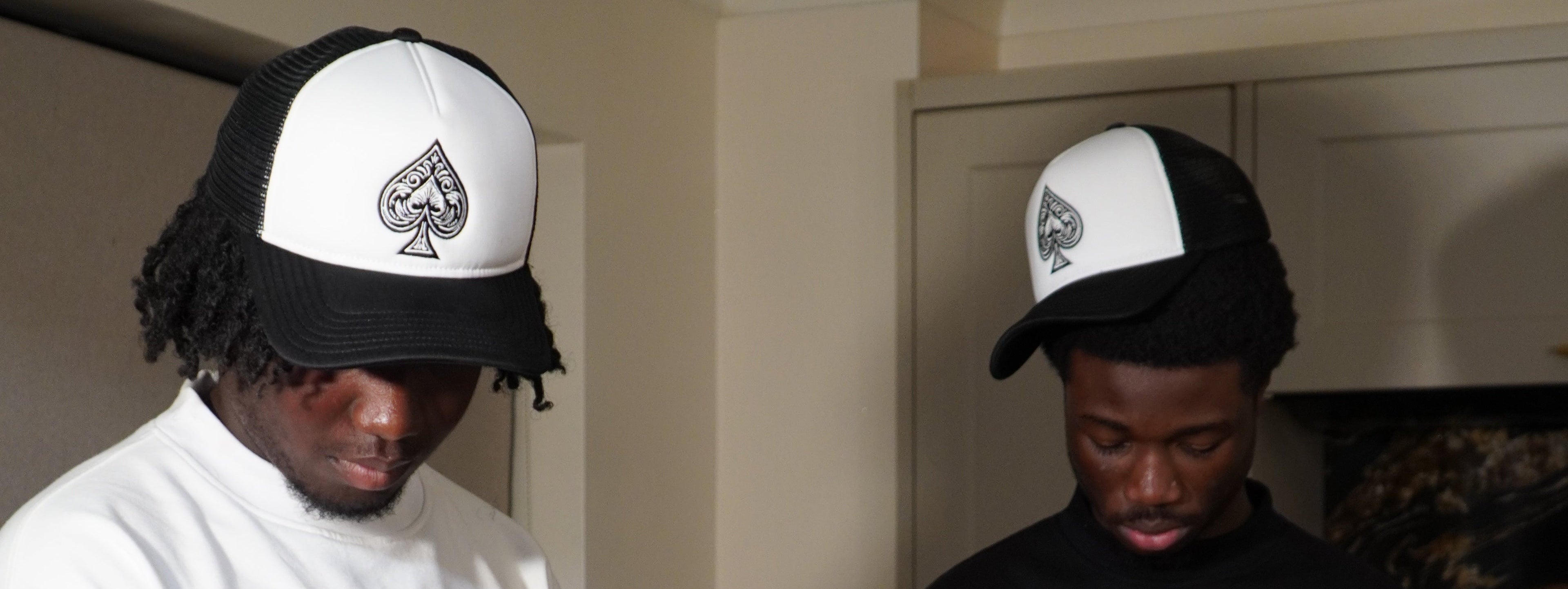 Two men wearing black and white caps with a spade symbol, one indoors and one outdoors.